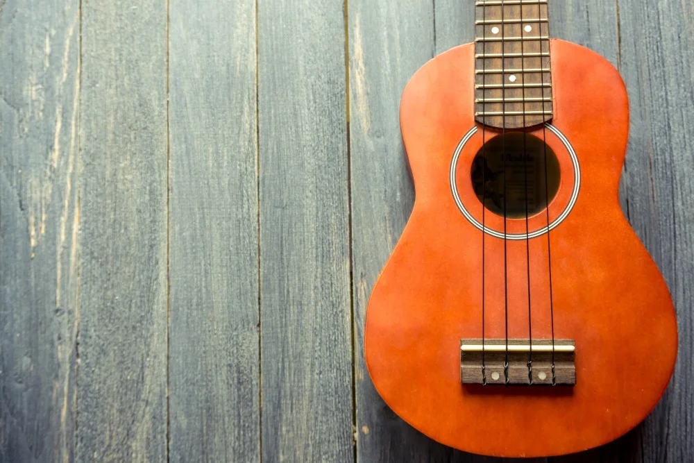 An orange ukulele is sitting on a wooden table, delivering the Perfect Sound.